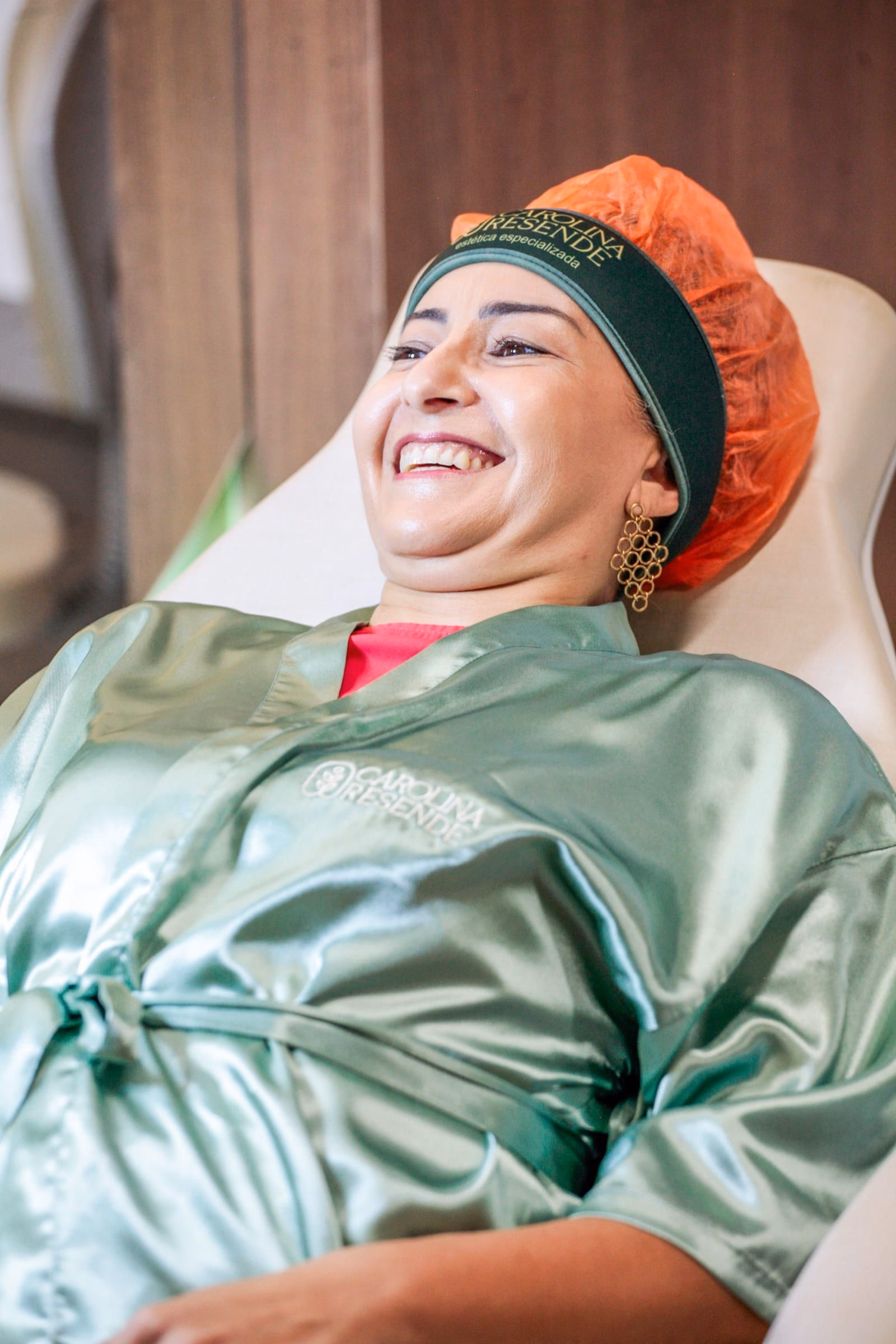 Dra. Carolina ajustando luminária durante atendimento, paciente sorrindo de roupão verde